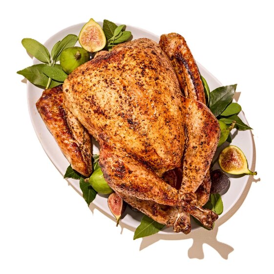 Roasted whole turkey on a platter with fresh figs and herbs, festive holiday dinner centerpiece.